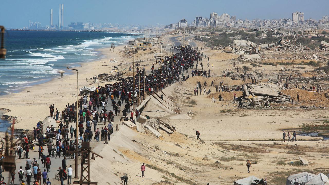 Eine breite Schlange von Menschen läuft einen Standstreifen inmitten des zerstörten Gazastreifens, links das Meer, hinten Ruinen von Gaza-Stadt.