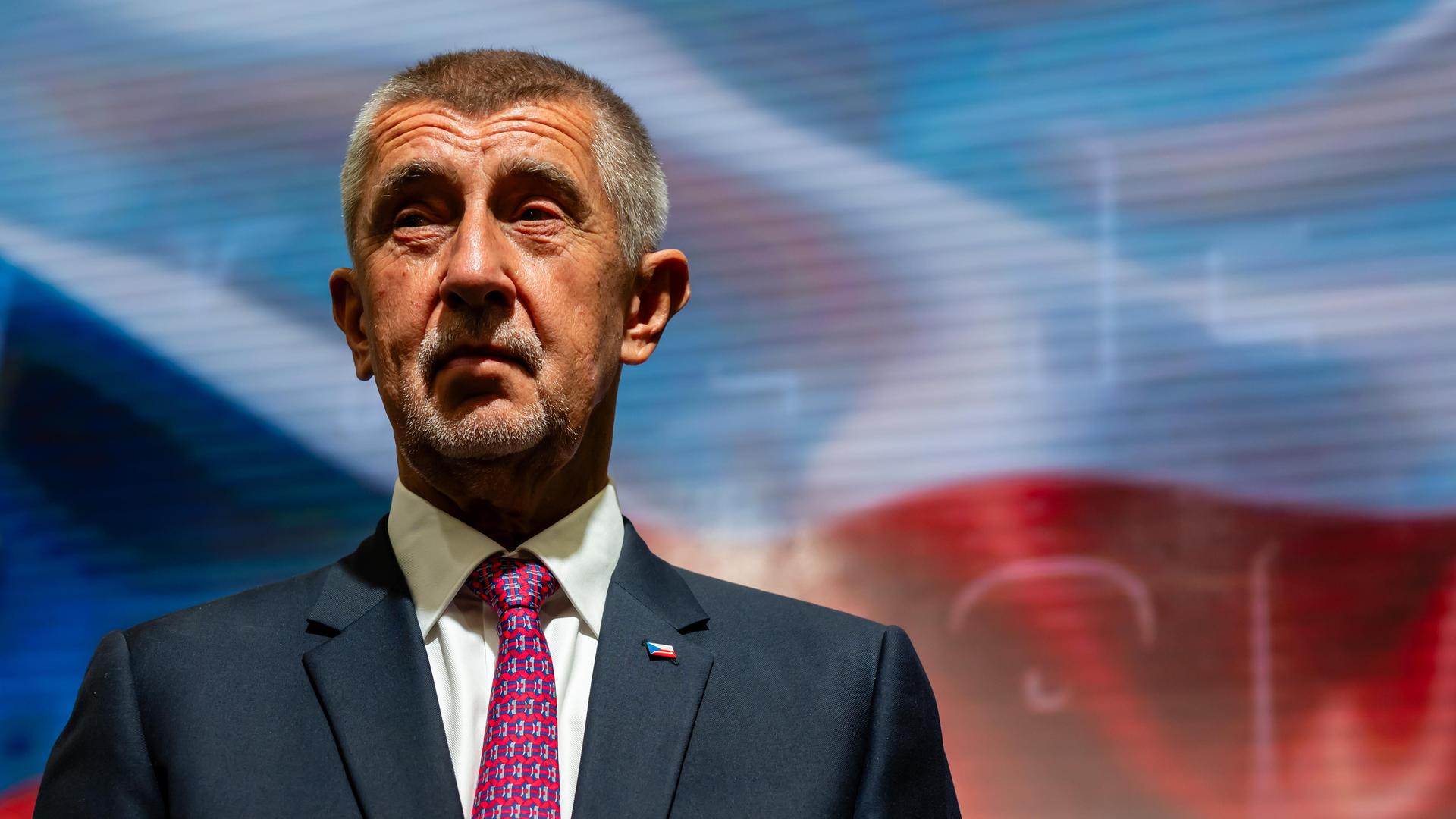 Portrait von Andrej Babiš in blauem Anzug, mit roter Krawatte vor der tschechischen Flagge