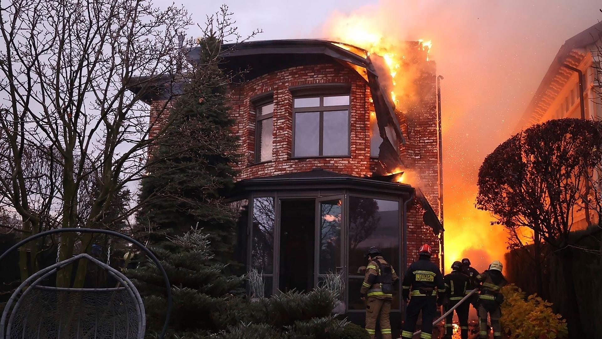 Ein brennendes Haus bei Nacht, was von Feuerwehrleuten in Schach gehalten wird Ein brennendes Haus bei Nacht, was von Feuerwehrleuten in Schach gehalten wird