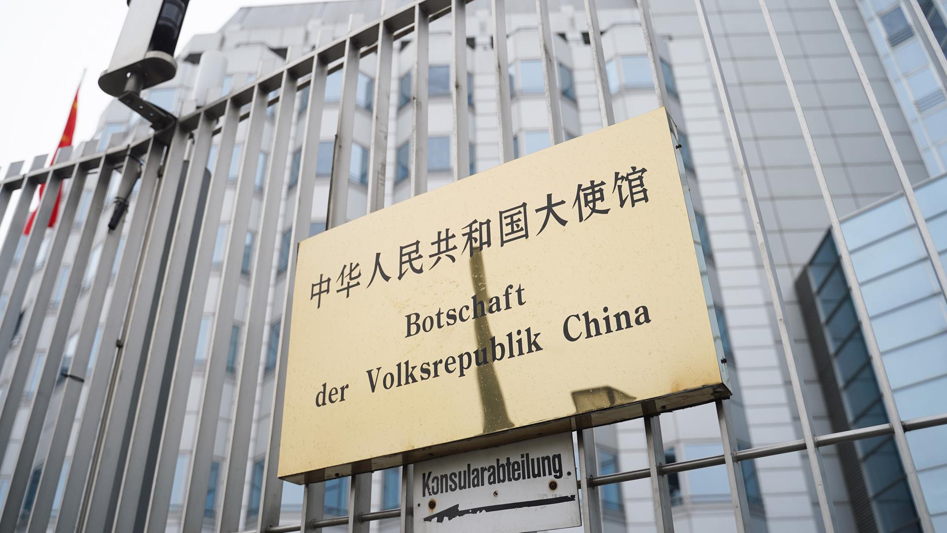 An einem Zaun ist ein Schild mit der Aufschrift "Botschaft der Volksrepublik China" befestigt.