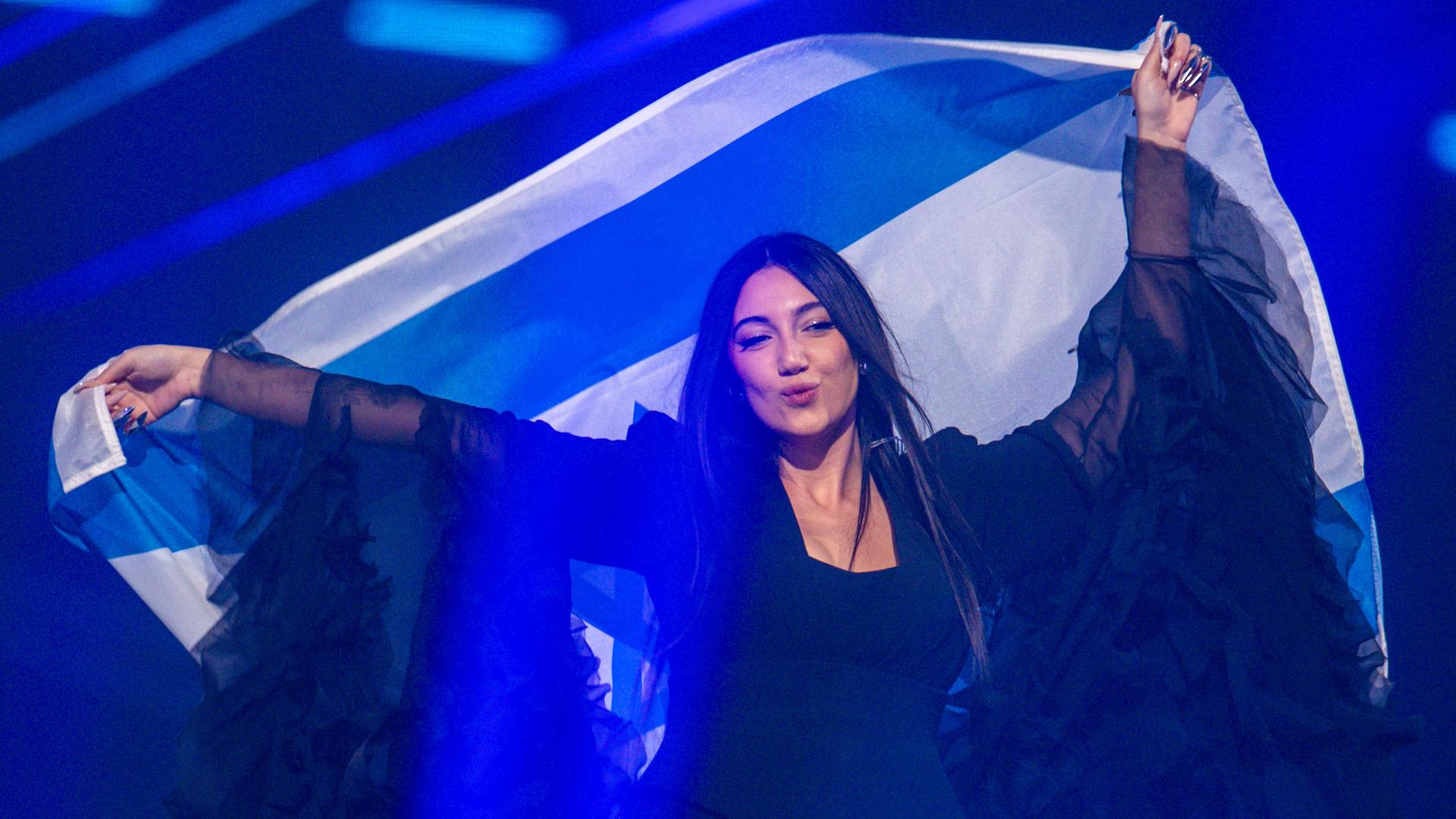 Die israelische ESC-Kandidatin Yuval Raphael steht auf einer Bühne und schwenkt eine israelische Fahne hinter ihrem Rücken.