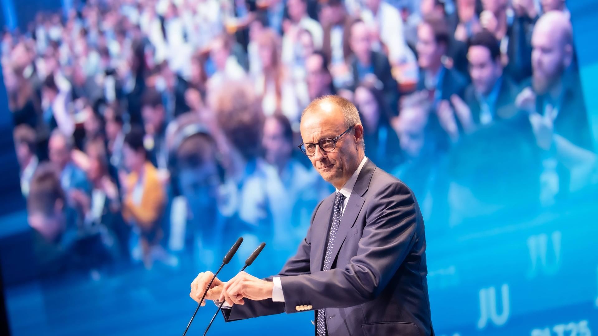 Friedrich Merz steht am Mikrofon, im Hintergrund sieht man zahlreiche Menschen.