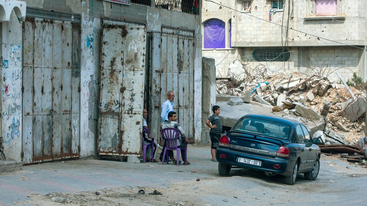 Zerstörte Häuser in Gaza Stadt an einer Zufahrtsstraße zu einem der zerstörten Stadtviertel. Ein Auto und drei Personen stehen daneben. 