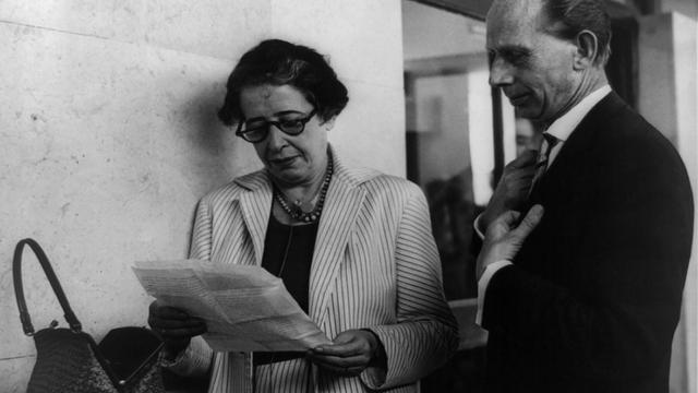 Ein Schwarz-weiß-Foto von circa 1960 zeigt Hannah Arendt, die mit Brille auf ein Blatt Papier schaut, neben ihr ein Reporter-Kollege Ein Schwarz-weiß-Foto von circa 1960 zeigt Hannah Arendt, die mit Brille auf ein Blatt Papier schaut, neben ihr ein Reporter-Kollege