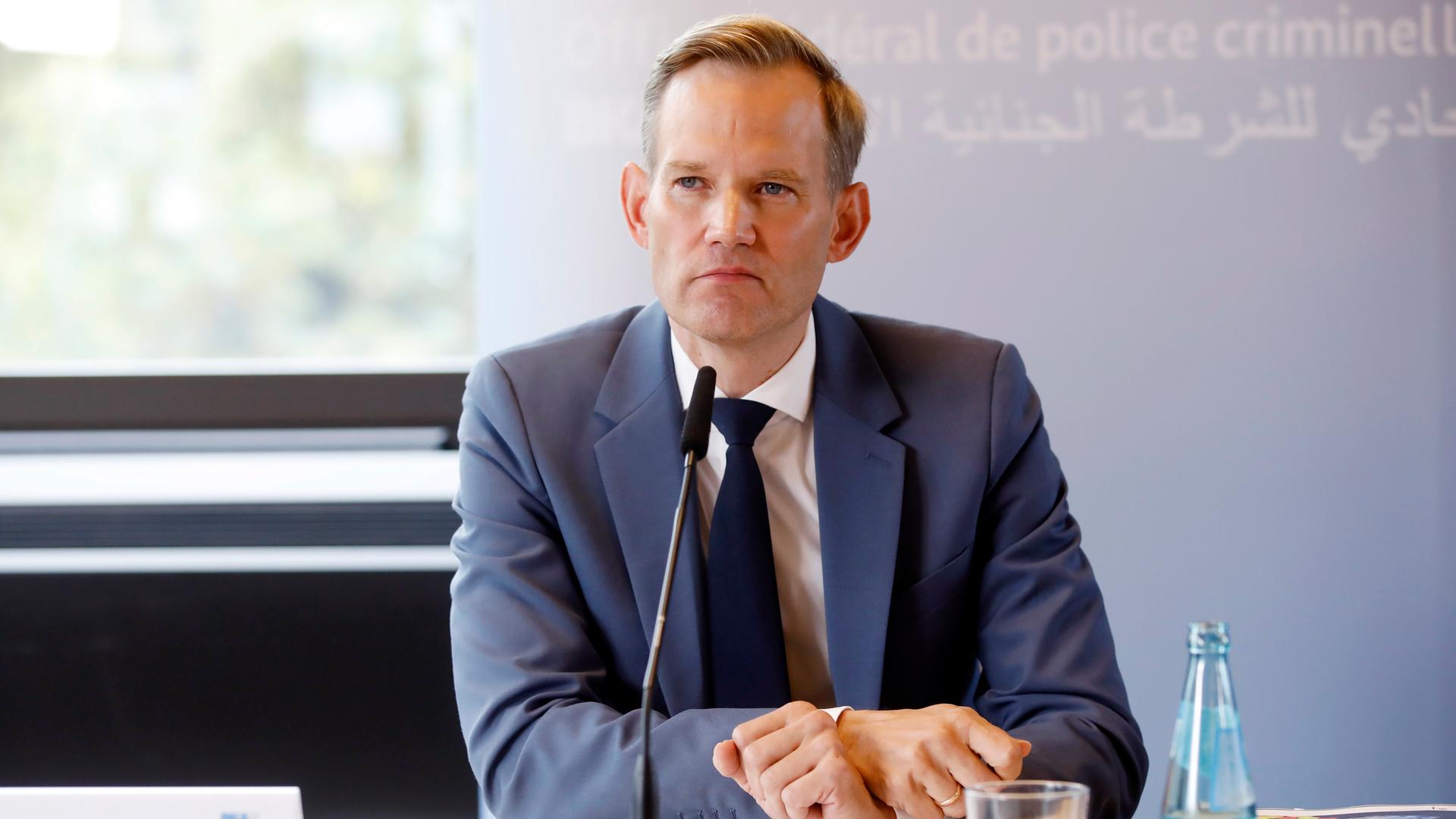 Ein Mann blick bei einer Pressekonferenz in die Kamera. Vor ihm ist ein Mikrofon. Er trägt einen dunklen Anzug, mit weißem Hemd und Kravatte. Es ist Hendrik Streeck, der Drogen- und Suchtbeauftragte der Bundesregierung.