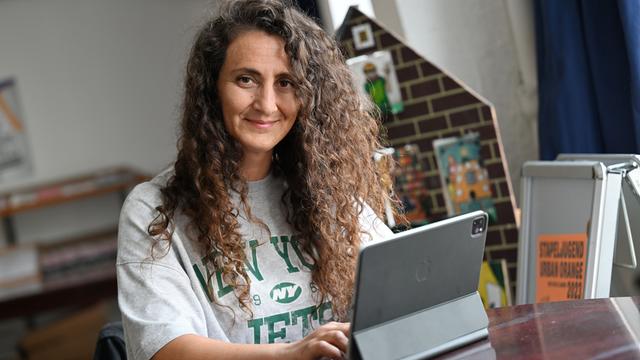 Lale Öztürk, eine Frau mit langen, lockigen Haaren, arbeitet an einem iPad. Lale Öztürk, eine Frau mit langen, lockigen Haaren, arbeitet an einem iPad.