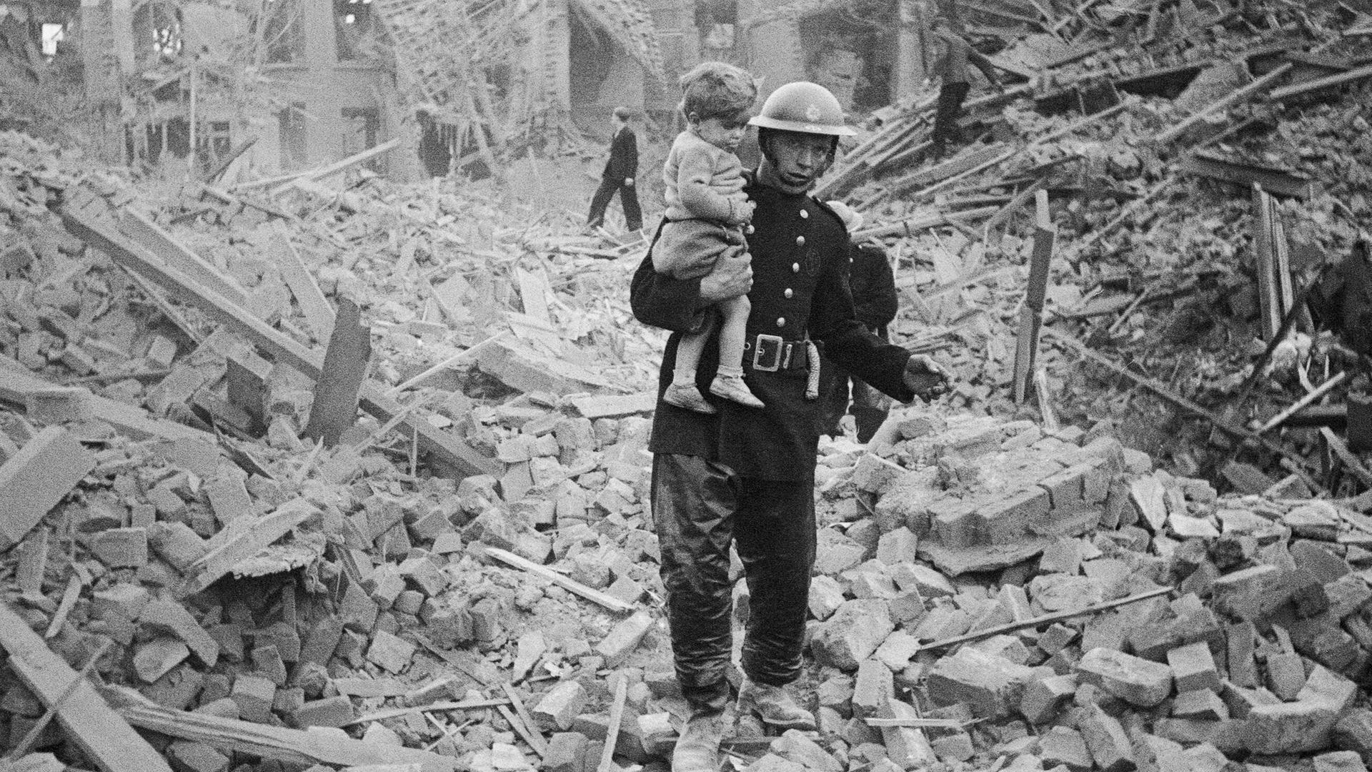 Ein Feuerwehrmann trägt ein Kleinkind nach einem Bombenangriff aus den Trümmern, London, um 1940. Ein Feuerwehrmann trägt ein Kleinkind nach einem Bombenangriff aus den Trümmern, London, um 1940.