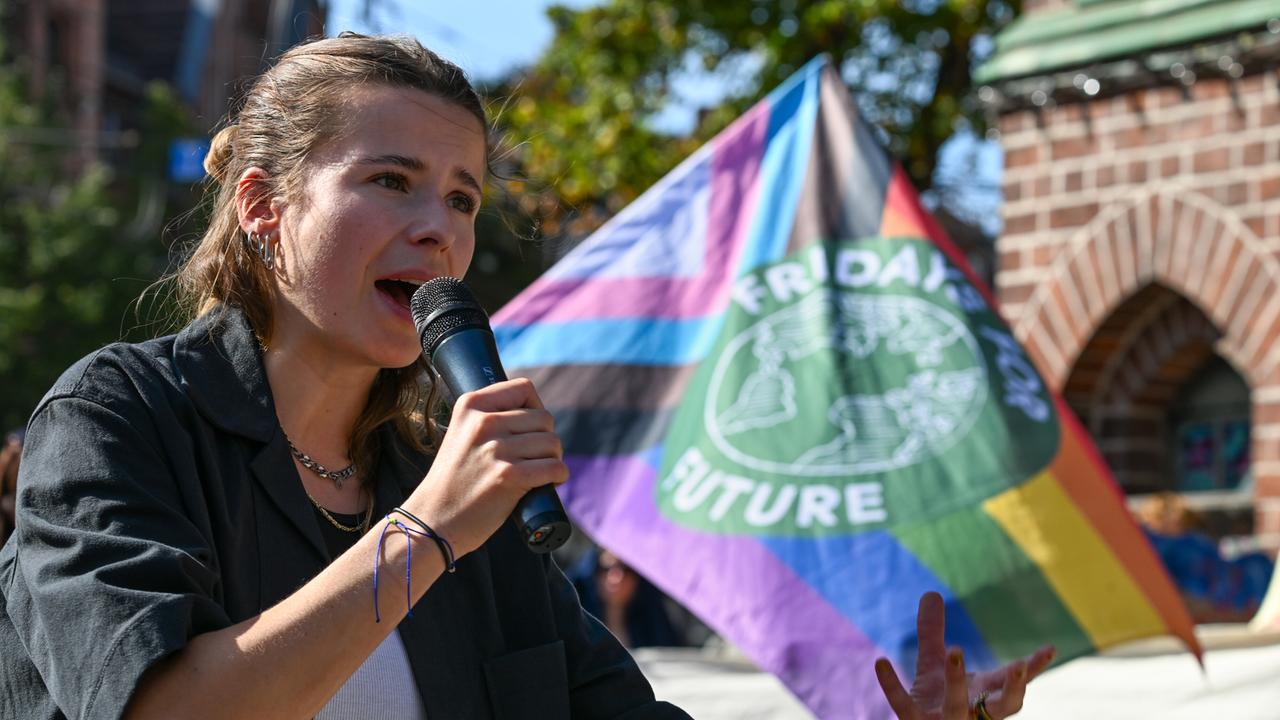 Luisa Neubauer von Fridays for Future spricht während einer Demonstration vor dem Babelsberger Rathaus. Sie trägt eine dunkle Bluse aus grobem Stoff und spricht in ein Mikrofon. Rechts im Bild die Flagge der Klimaschutzbewegung.