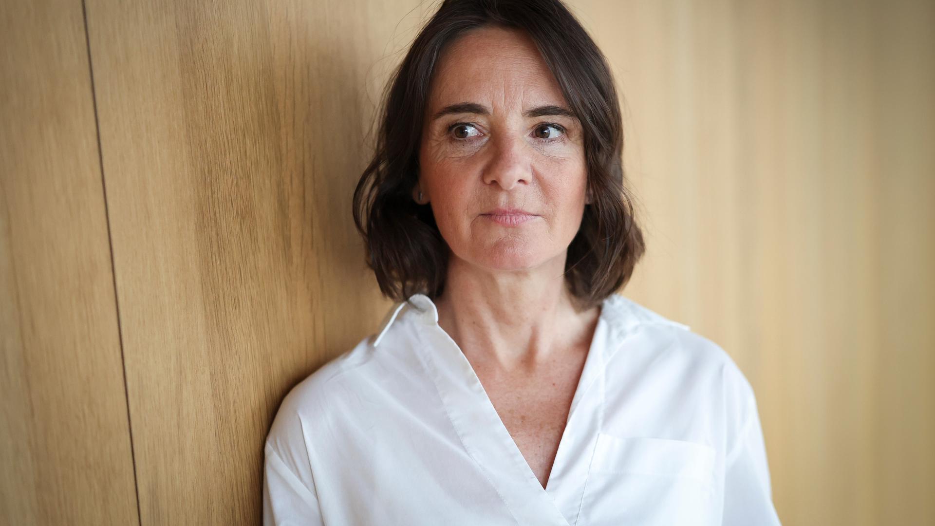 Martina Heßler mit weißer Bluse und dunklen Haaren steht vor einer Wand aus Holz und schaut zur Seite