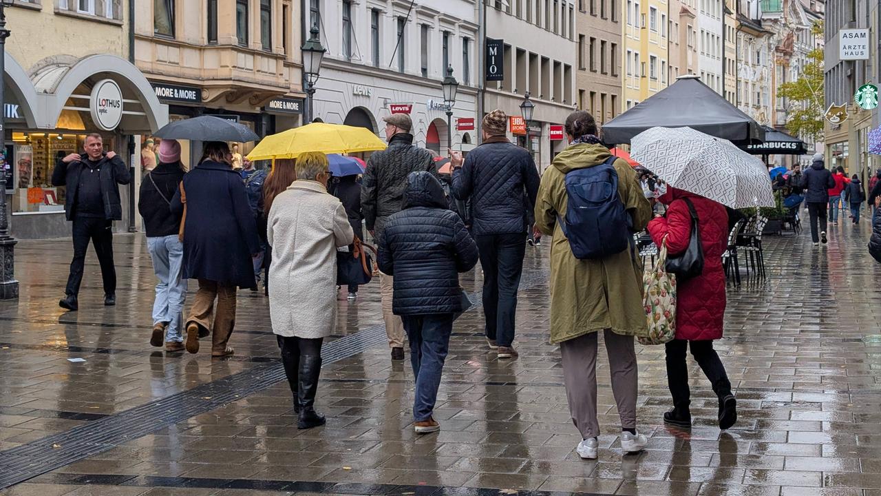 Menschen mit Regenschirmen gehen durch eine Münchener Fußgängerzone