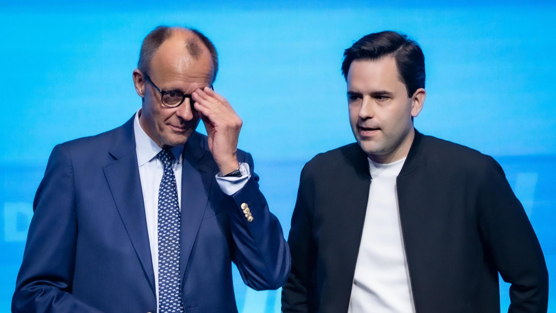 Bundeskanzler Friedrich Merz steht neben Johannes Winkel, Bundesvorsitzender Jungen Union, und fasst sich an die Brille, beide sehen nicht sehr glücklich aus Bundeskanzler Friedrich Merz steht neben Johannes Winkel, Bundesvorsitzender Jungen Union, und fasst sich an die Brille, beide sehen nicht sehr glücklich aus