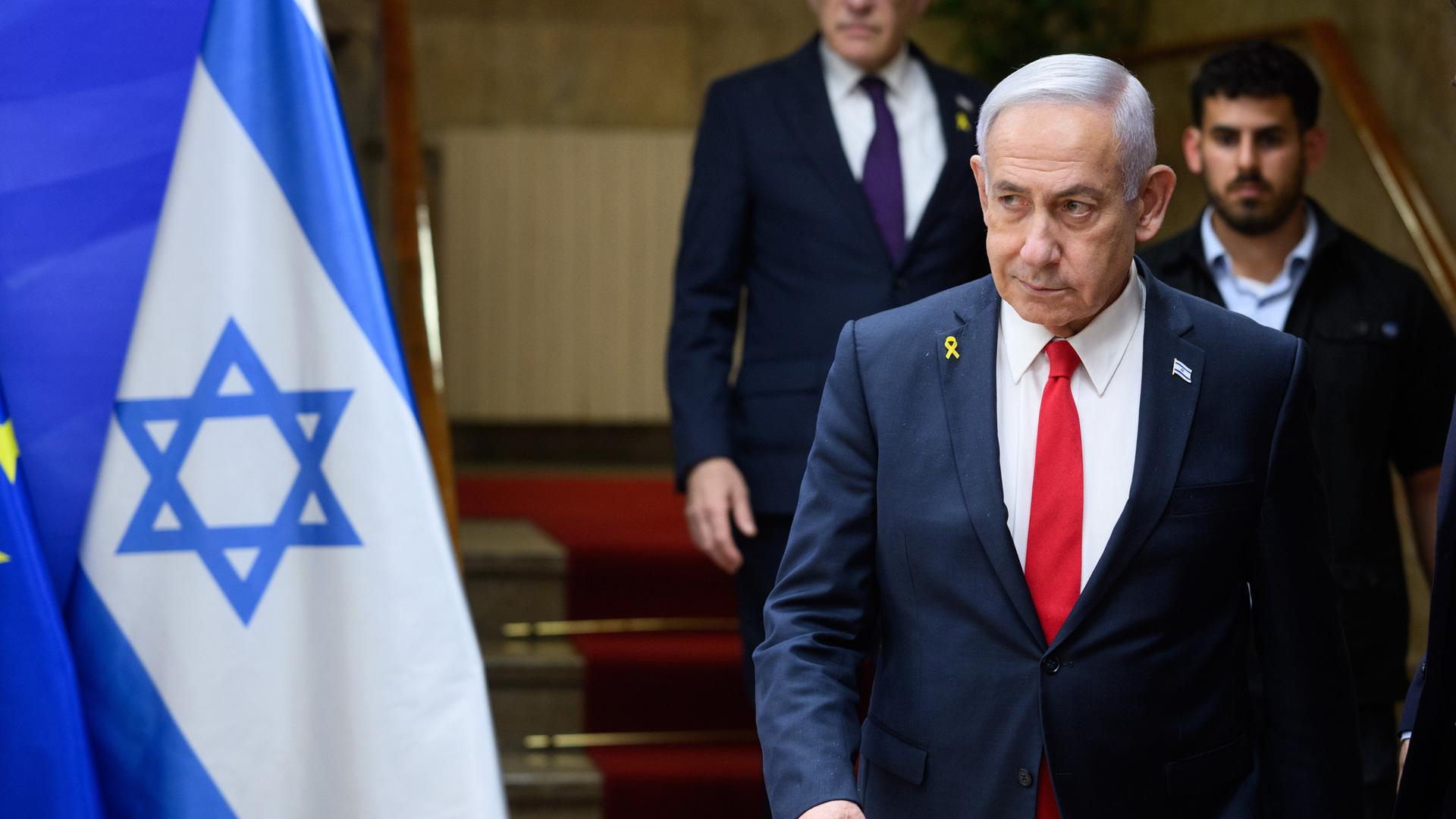 Benjamin Netanjahu, Ministerpräsident von Israel, läuft eine Treppe hinunter, ein Personenschützer ist hinter zu sehen. Neben ihm ist die Flagge Israels zu erkennen.