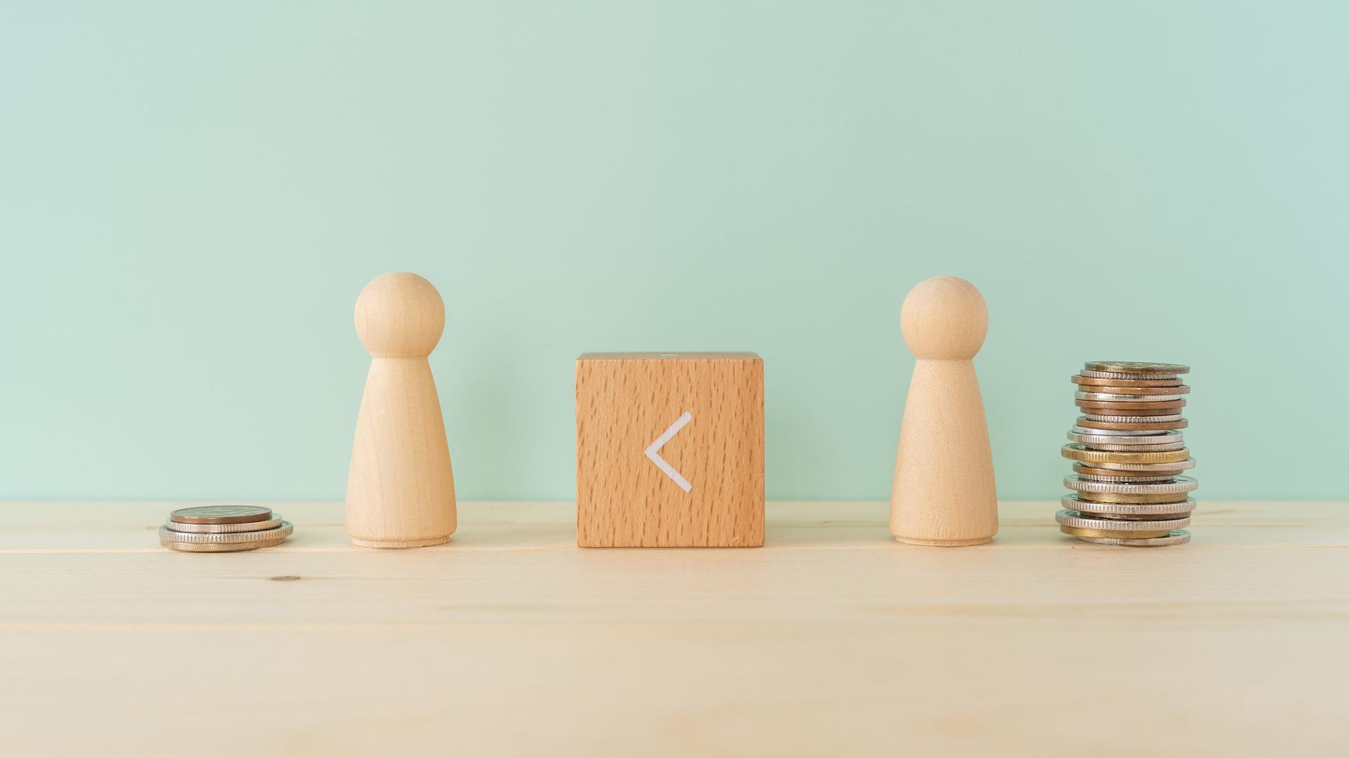 Zwei Spielfiguren aus Holz stehen auf einem Tisch. Dazwischen ein Holzklötzchen, auf dem das
Größer-als-Zeichen zu sehen ist, es zeigt nach links. Neben der linken Figur stapeln sich vier Geldstücke, neben der rechten Figur deutlich mehr.
Zwei Spielfiguren aus Holz stehen auf einem Tisch. Dazwischen ein Holzklötzchen, auf dem das
Größer-als-Zeichen zu sehen ist, es zeigt nach links. Neben der linken Figur stapeln sich vier Geldstücke, neben der rechten Figur deutlich mehr.
