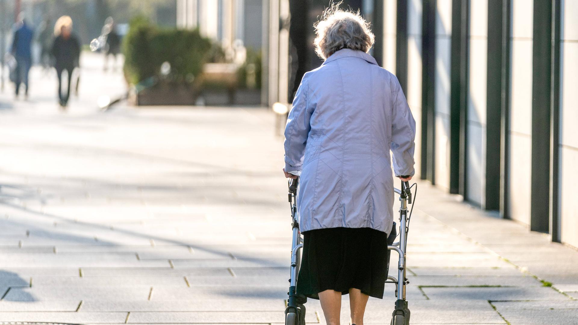 Eine Seniorin läuft am Rollator durch eine Fussgängerzone. (Rückenansicht)