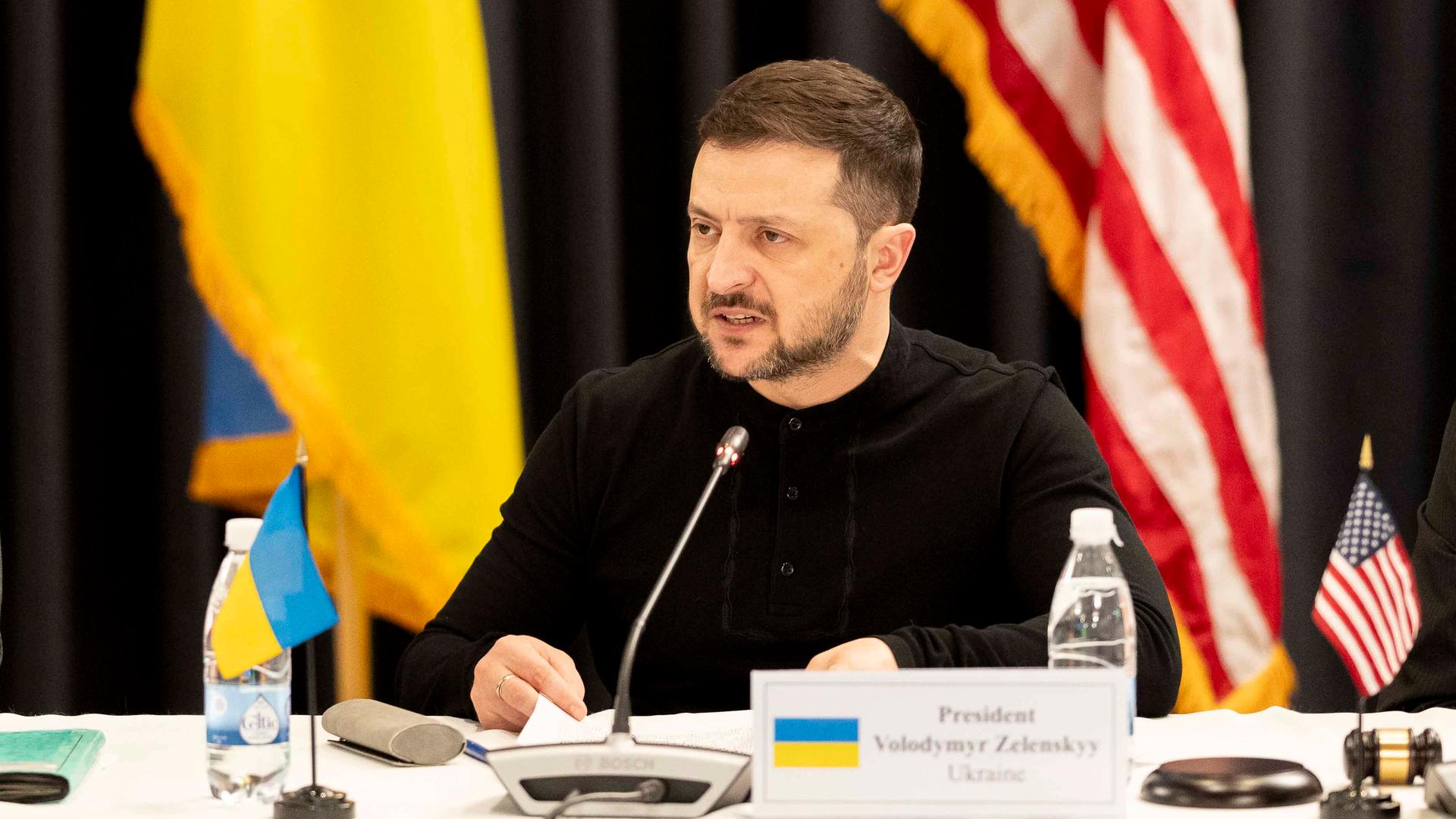 Der ukrainische Präsident Selenskyj sitzt beim Treffen der Ukraine-Partner in Ramstein an einem Tisch, neben sich die Flagge der Ukraine sowie die US-Flagge, und hält mit wütendem Gesichtsausdruck eine Rede. Der ukrainische Präsident Selenskyj sitzt beim Treffen der Ukraine-Partner in Ramstein an einem Tisch, neben sich die Flagge der Ukraine sowie die US-Flagge, und hält mit wütendem Gesichtsausdruck eine Rede.