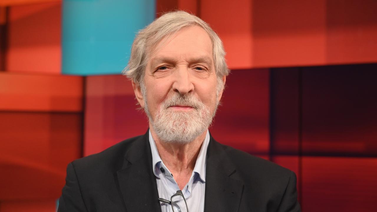 Shimon Stein sitzt in einem Fernsehstudio mit rot gekacheltem Hintergrund
