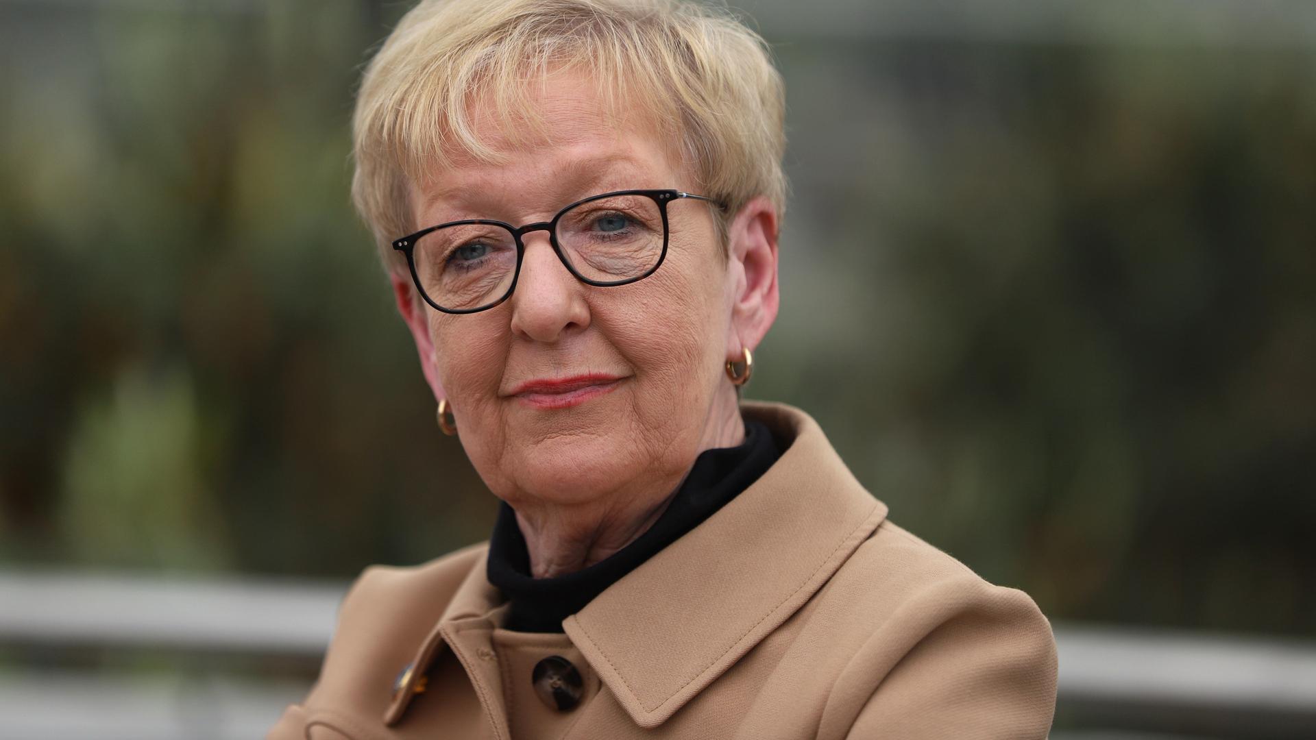 Stefanie Babst trägt einen hellbraunen Mantel, eine schwarz umrandete Brille und scheint interessiert in die Kamera Stefanie Babst trägt einen hellbraunen Mantel, eine schwarz umrandete Brille und scheint interessiert in die Kamera