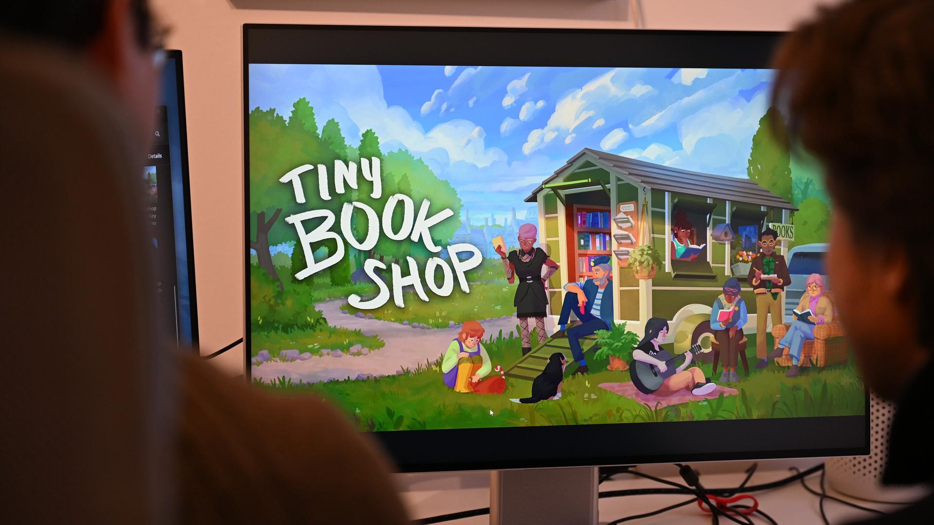 Zwei junge Männer sitzen vor einem Screen und blicken auf das Game "Tiny Bookshop".
